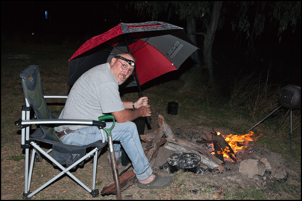 The dedicated cook keeping the wind and rain off the camp oven during the storm.